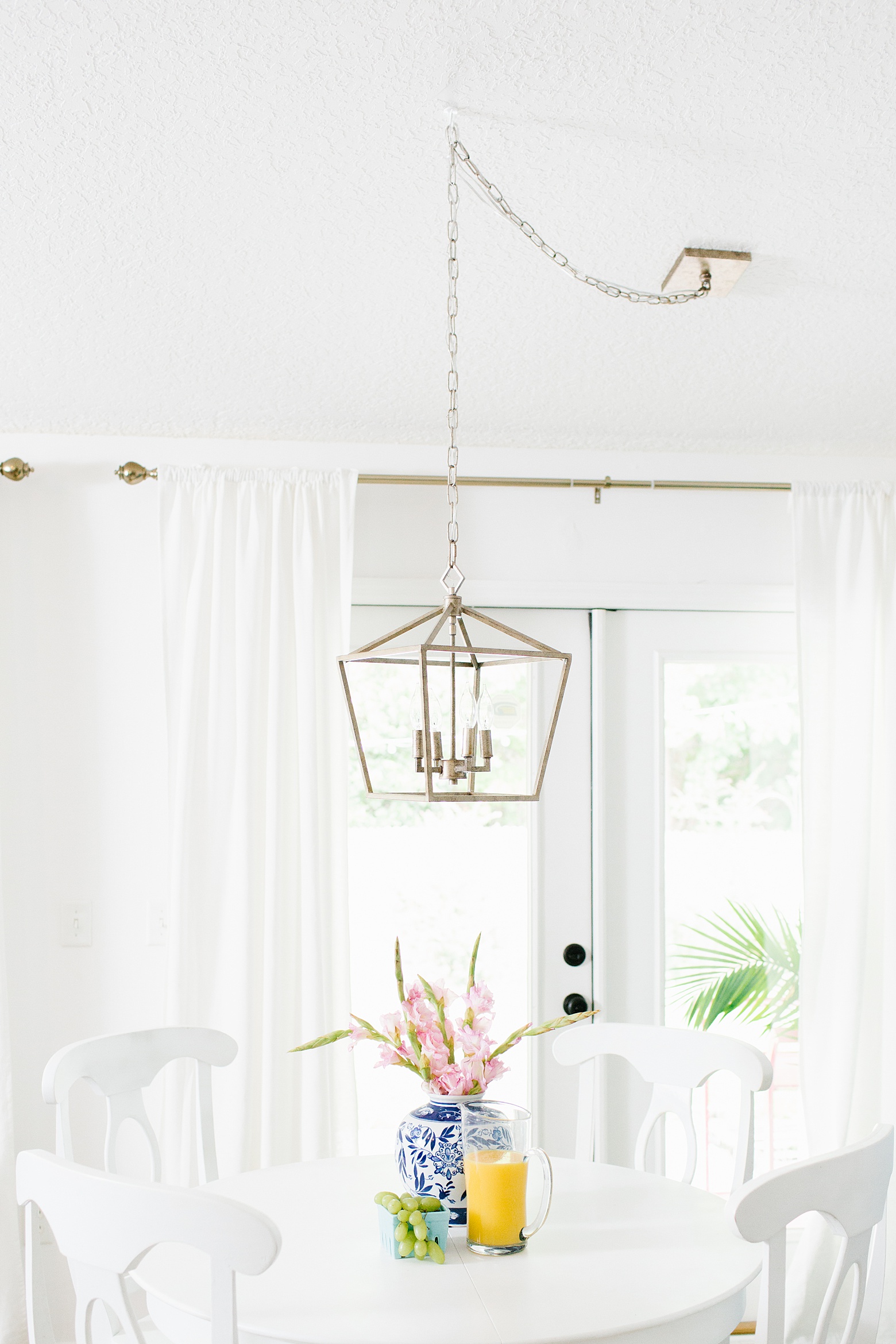 All bright white kitchen nook featuring a gold cage lantern pendant by Lighting Connection, white walls, white curtains, white and gold kitchen